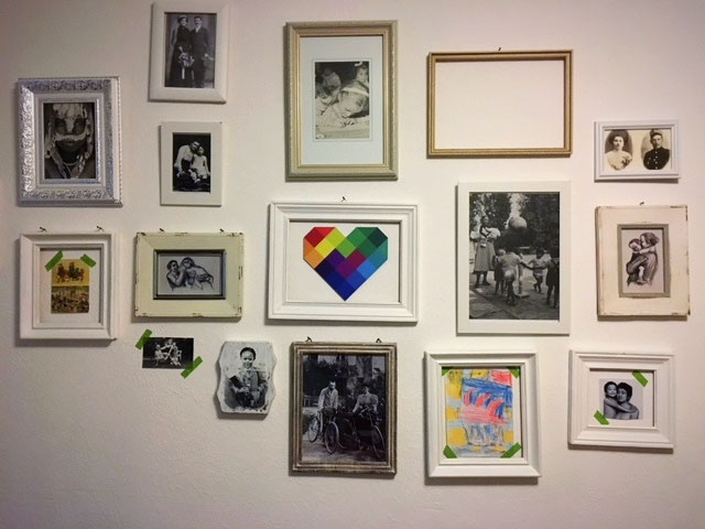 Wand mit gerahmten Familienfotos und einem bunten Regenbogenherz in der Mitte